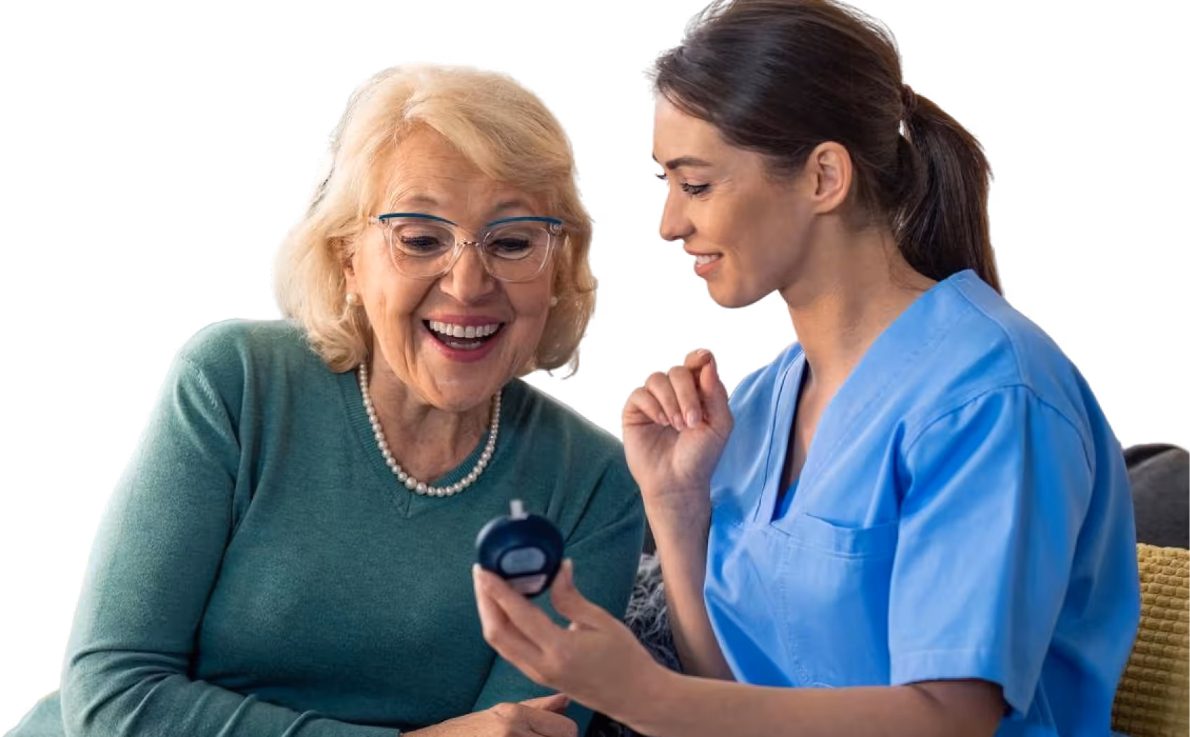 Nurse in blue scrubs showing a device to a happy elderly woman in glasses and a green sweater.