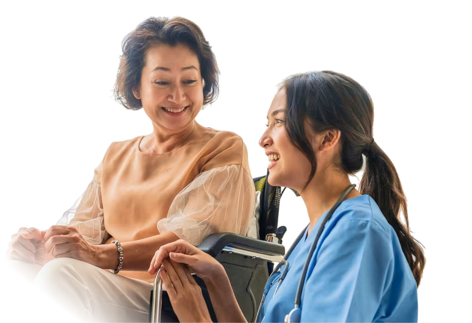 Smiling nurse in blue scrubs holding hands with a seated elderly woman in a wheelchair.