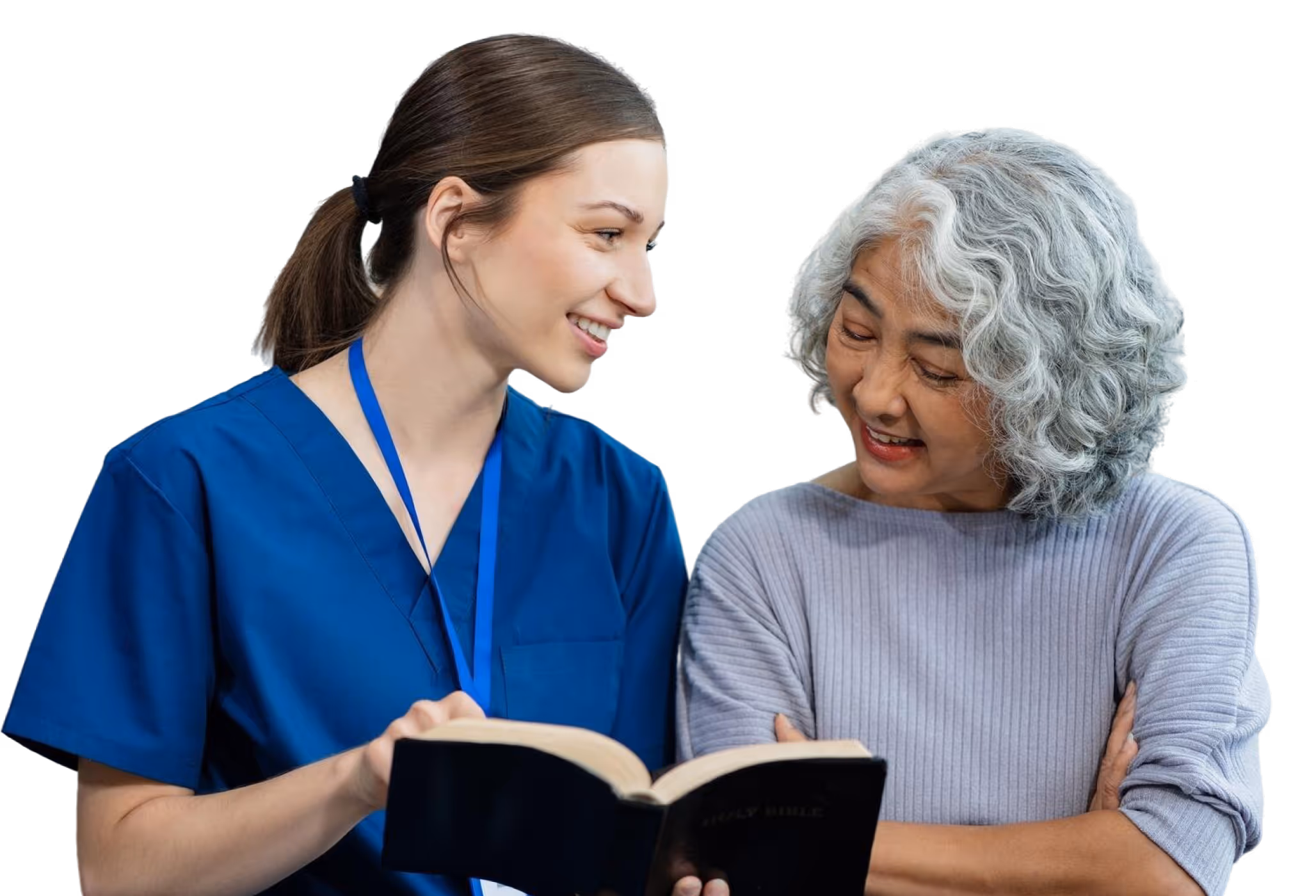 Healthcare worker in blue scrubs showing a book to a smiling elderly woman with gray hair.
