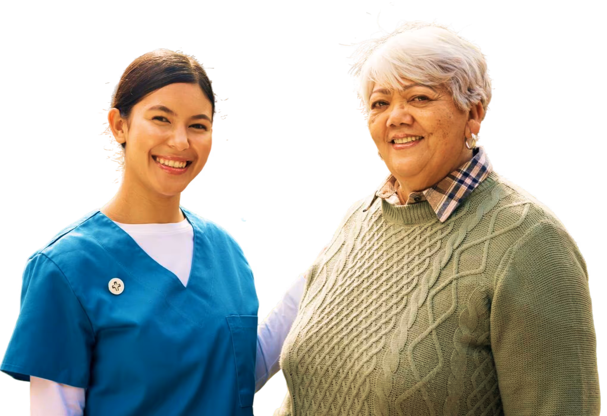 Smiling nurse in blue scrubs standing next to a happy elderly woman in a green sweater.