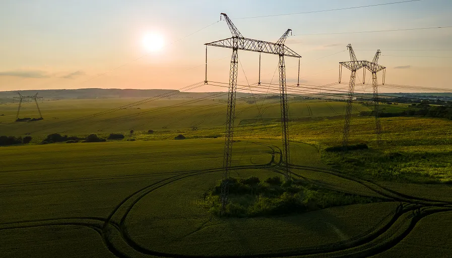Electrical power lines on tall metal towers crossing green fields under a setting sun.