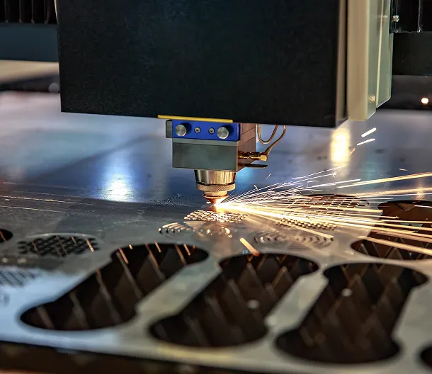 Laser cutting machine emitting sparks while cutting a metal sheet with intricate patterns.
