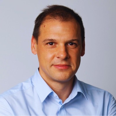 Smiling middle-aged man with short hair and light stubble wearing a white shirt.