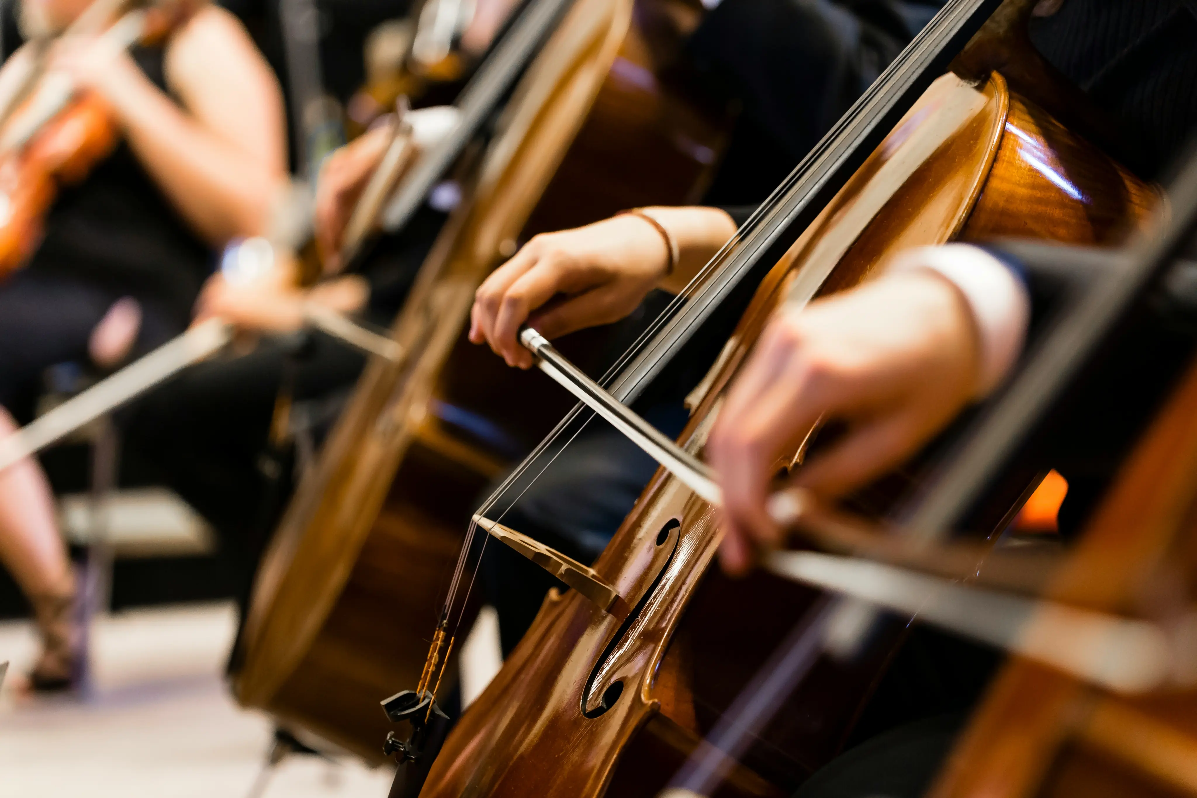Close-up of musicians playing cellos with bows in an orchestra setting.