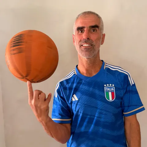 Man spinning an orange basketball on his fingertip wearing blue Italy soccer jersey.