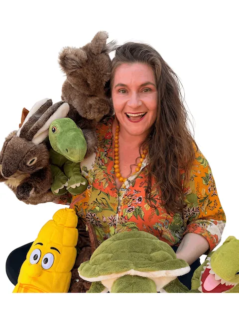 Ricky Roo & Friends entertainer Amina holding various plush toys including a turtle, corn, rabbit, and dinosaur.