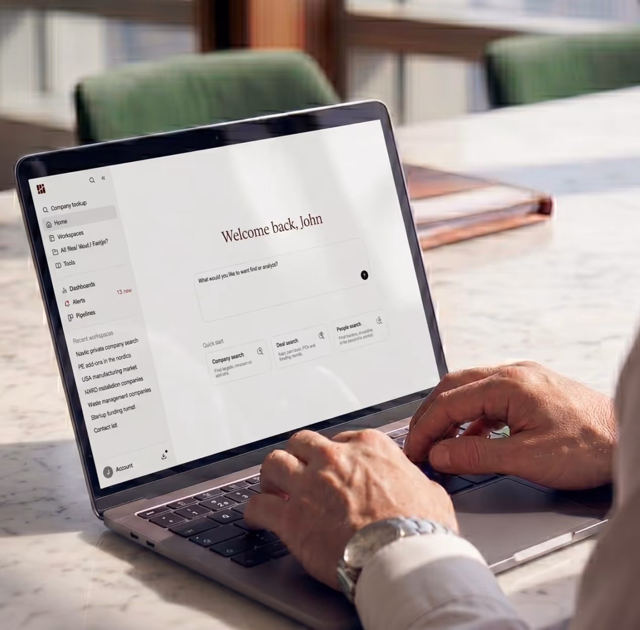 Person typing on a laptop displaying a dashboard with a 'Welcome back, John' message and search options.