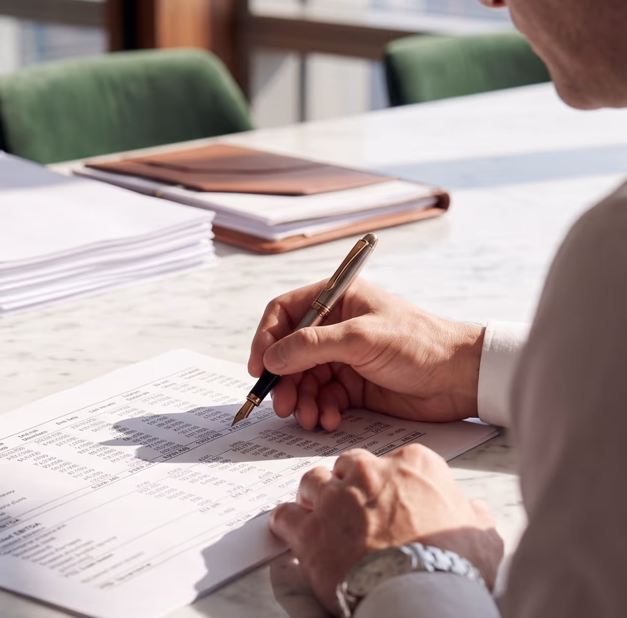 Person reviewing a printed financial report with a pen over a marble desk in bright daylight.