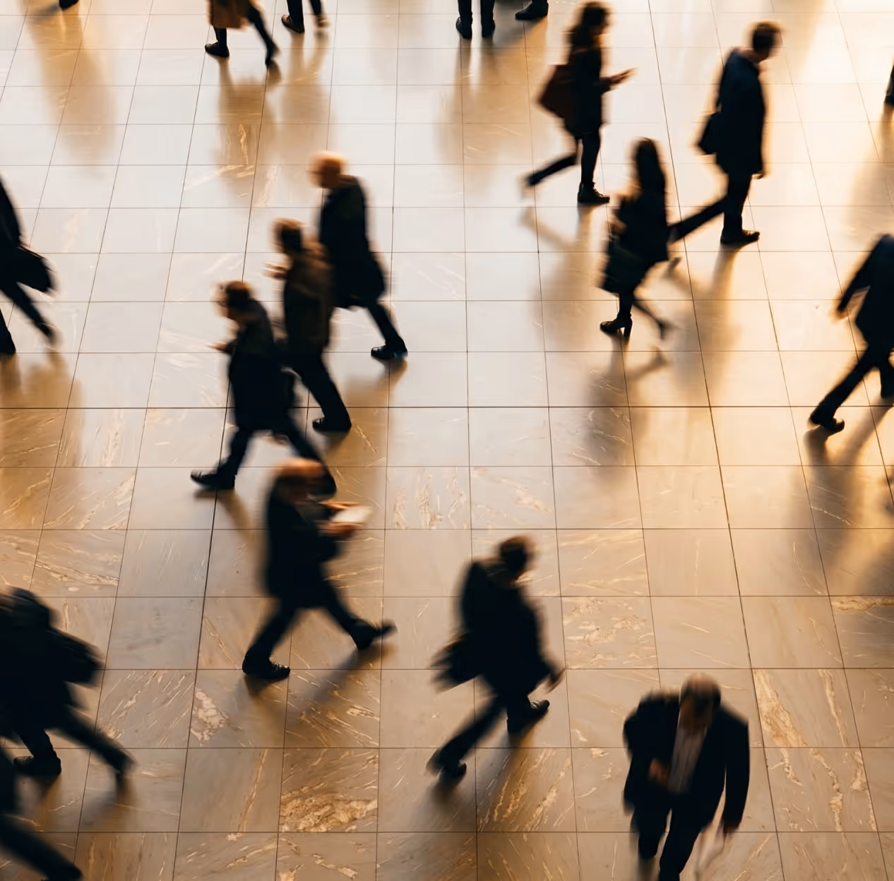Blurred overhead view of people walking on a shiny tiled floor in a public space.