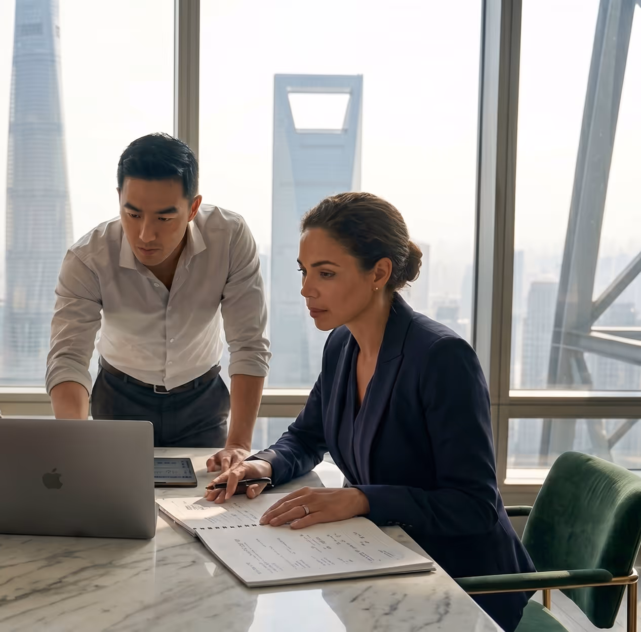Two business professionals reviewing notes and laptop at a marble table in a high-rise office.