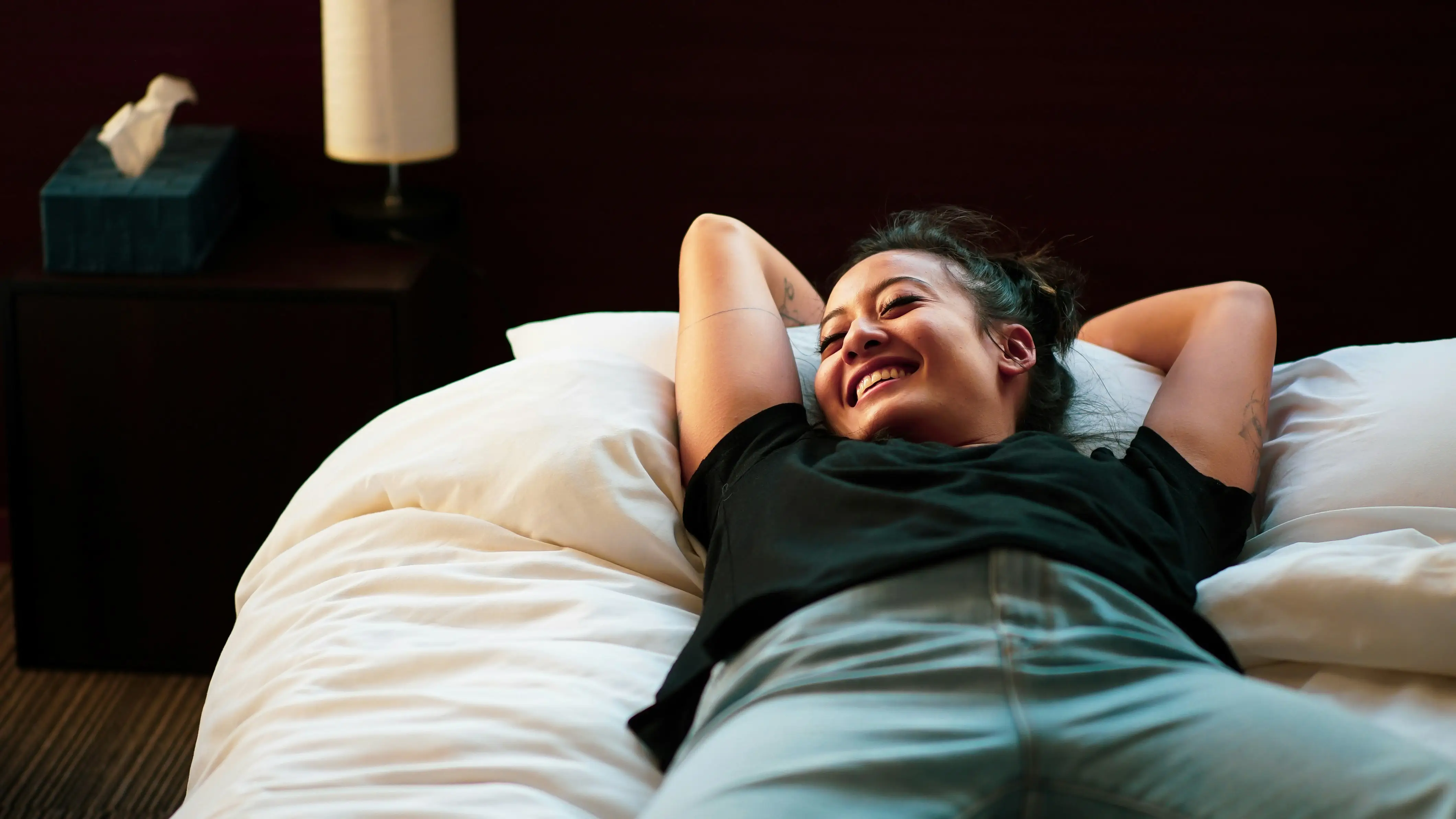 Femme souriante allongée sur un lit avec les bras derrière la tête.