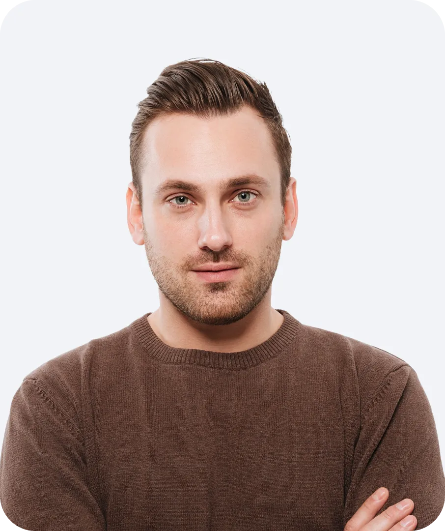Portrait of a man with light skin and short brown hair, wearing a brown sweater and looking directly at the camera with arms crossed.