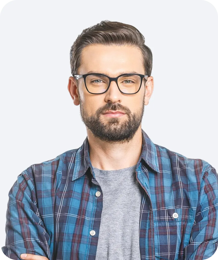 Man with glasses and beard wearing a blue plaid shirt over a gray t-shirt, standing with arms crossed.
