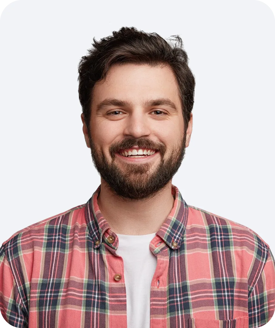 Smiling young man with dark hair and beard wearing a red plaid shirt and white t-shirt.