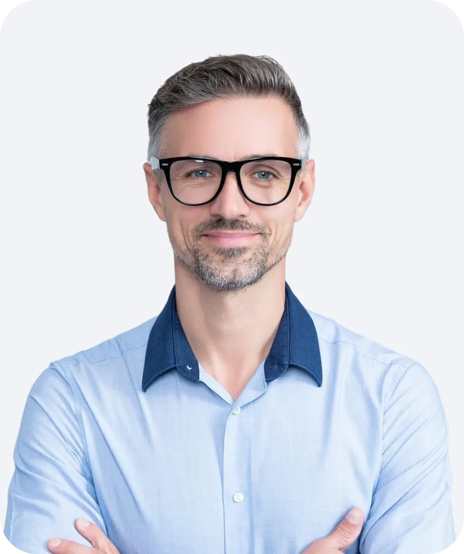 Smiling middle-aged man with gray hair and beard wearing black glasses and a light blue shirt with dark blue collar.