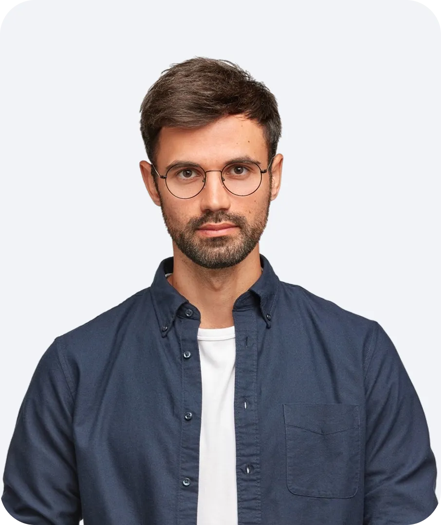 Portrait of a serious young man with glasses, short dark hair, and beard wearing a navy blue shirt over a white t-shirt.
