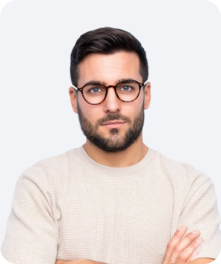Man with short dark hair, beard, and round tortoiseshell glasses wearing a light beige knit shirt with arms crossed.