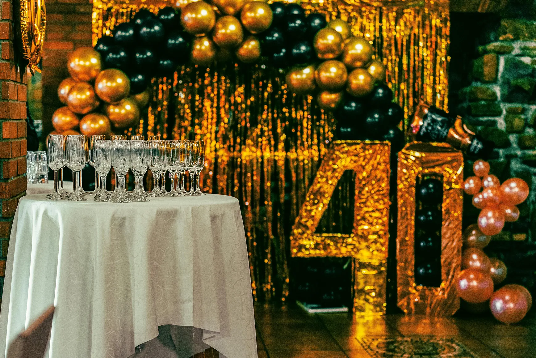 Ein festlich dekorierter Tisch mit leeren Weingläsern vor goldenen und schwarzen Luftballons und einer großen goldenen 40-Deko.