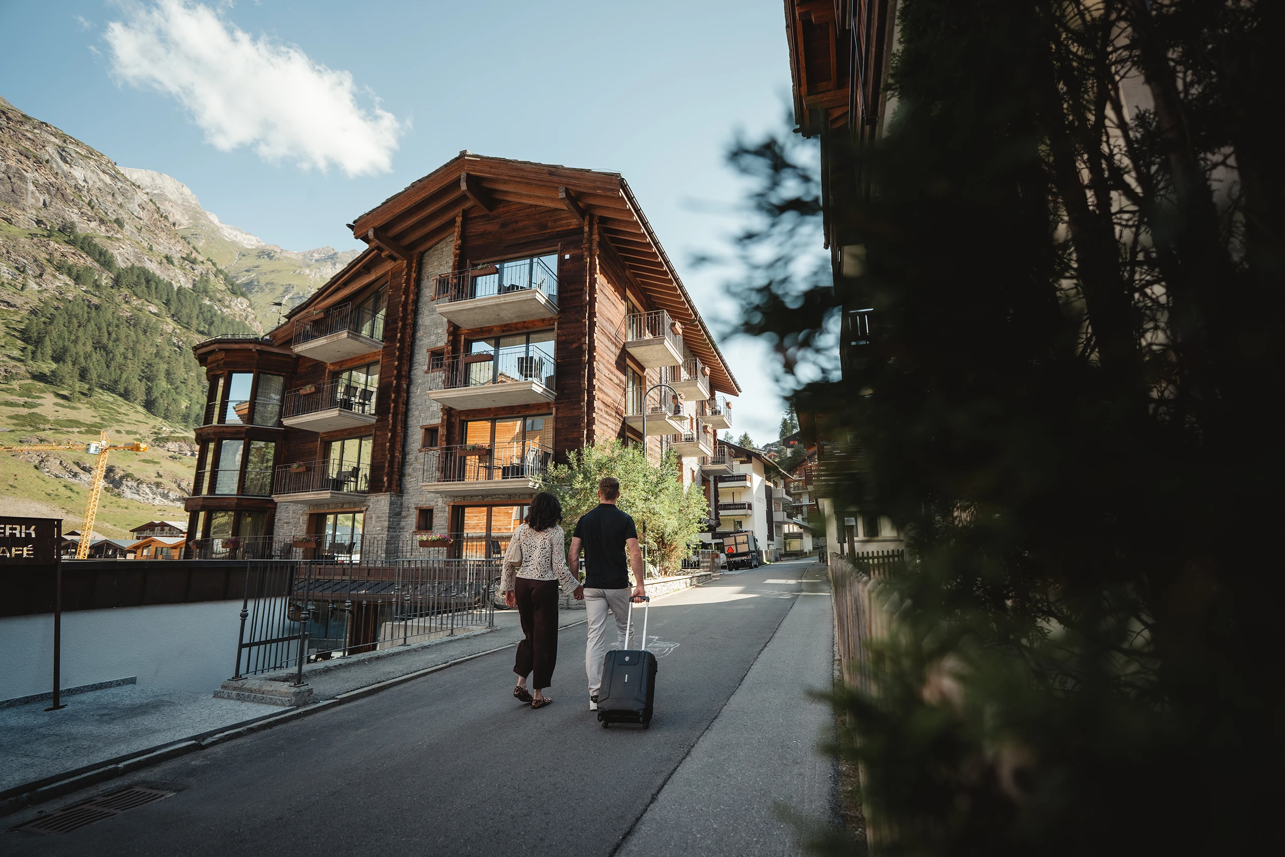 Paar mit Koffer vor dem Hotel Phoenix Zermatt, im Hintergrund die Walliser Bergwelt