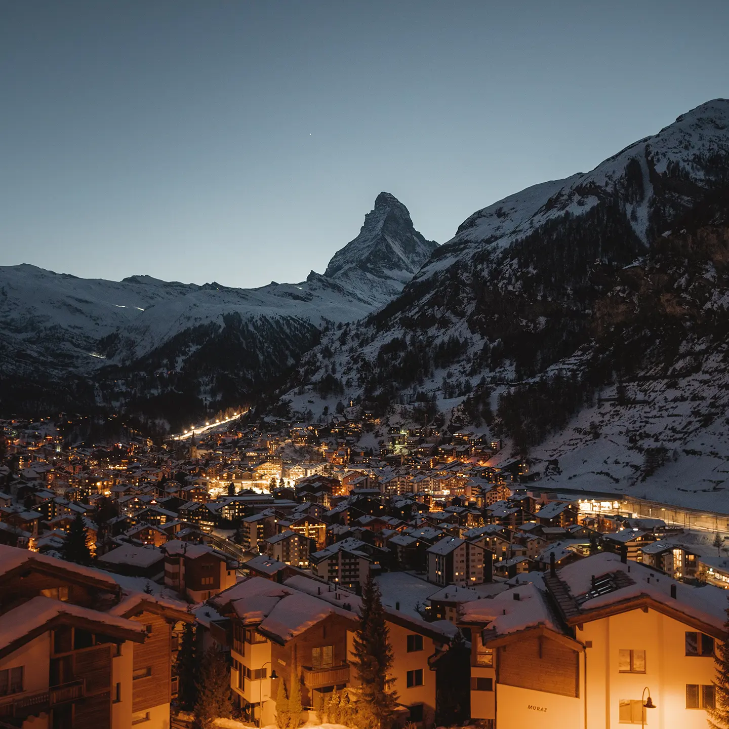 Zermatt bei Dämmerung mit beleuchteten Chalets und dem Matterhorn im Hintergrund
