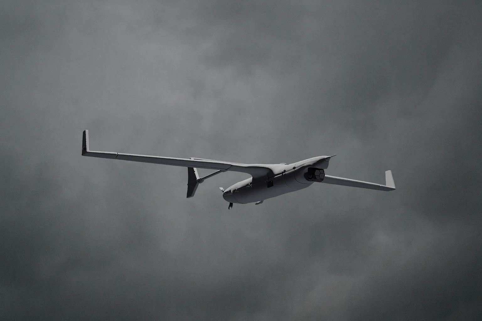 Small unmanned drone flying against a cloudy gray sky.