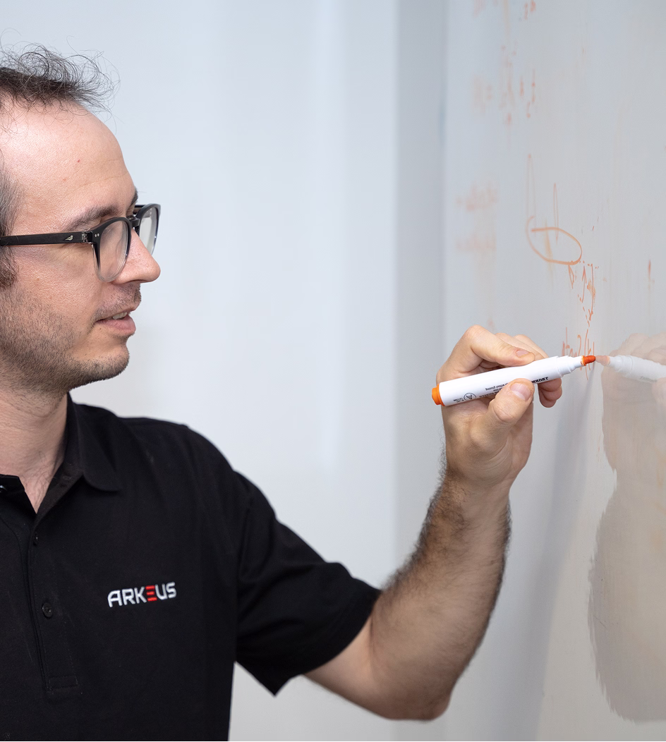 Man in glasses writing with an orange marker on a whiteboard.