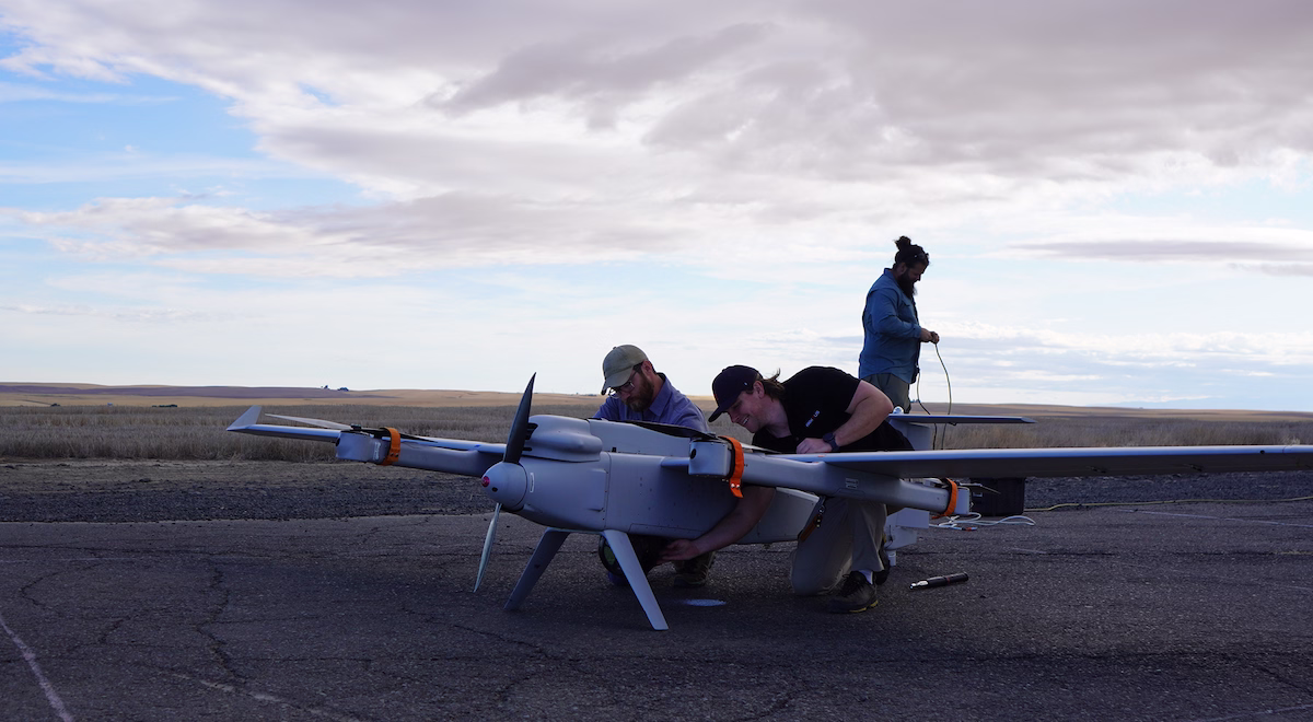 Three men preparing a large drone on a paved surface under a cloudy sky.