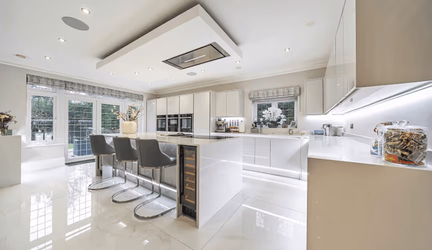 Bright modern white kitchen with large island, three gray bar stools, and glass doors leading outside.