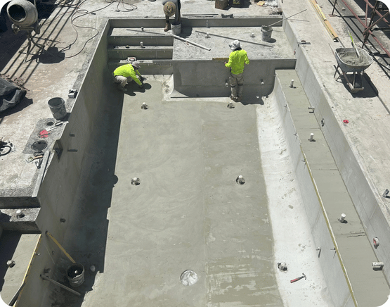 Two construction workers applying finishing touches to a concrete pool under construction.