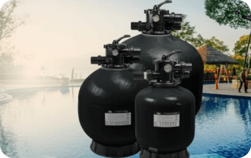 Three black pool filter tanks of different sizes positioned near a swimming pool outdoors.