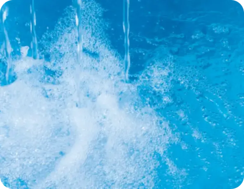 Clear water being poured into a pool of blue water creating white foam and bubbles.