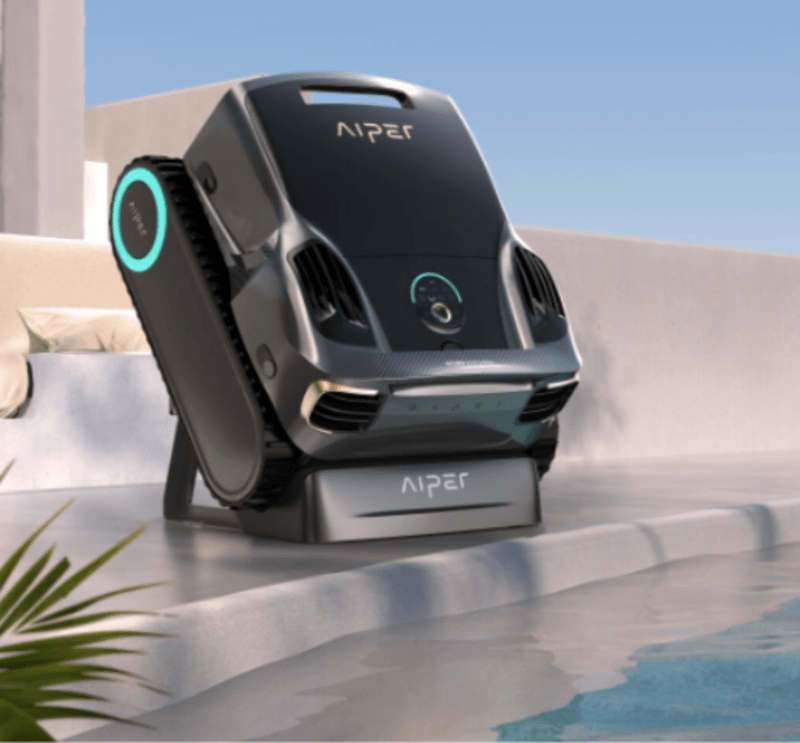 Black and gray robotic pool cleaner with tracks on a poolside ledge near water.