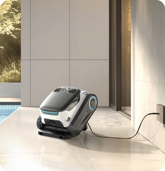 Robotic pool cleaner charging on a tiled floor near a modern outdoor pool area.