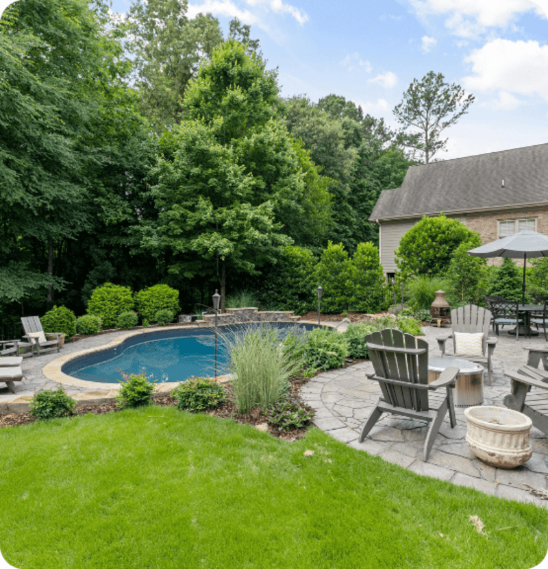 Backyard with a kidney-shaped pool, patio with chairs, and lush green trees and grass.
