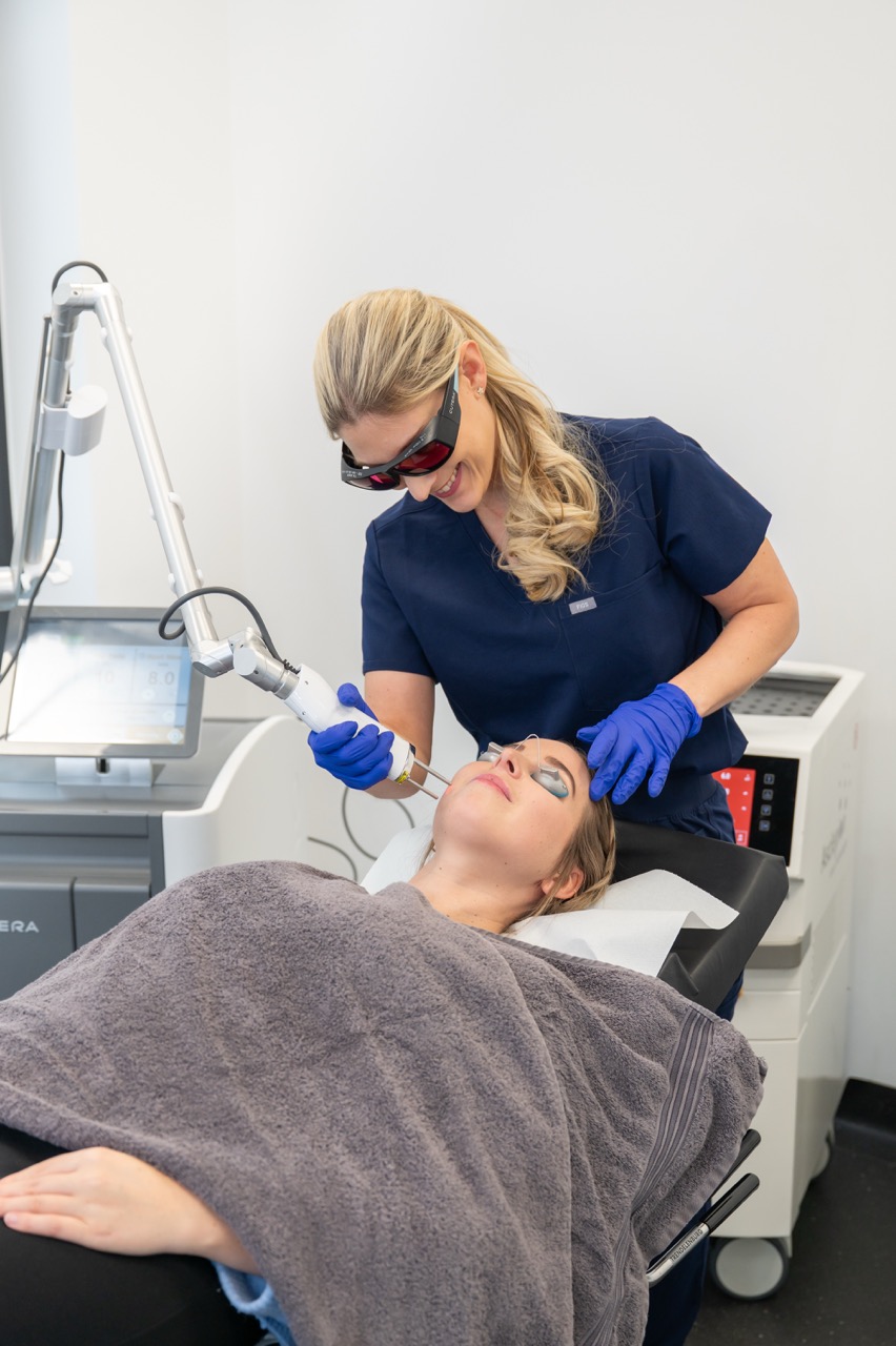 Ärztin behandelt Frau mit Lasergerät im Gesicht in moderner Klinik.