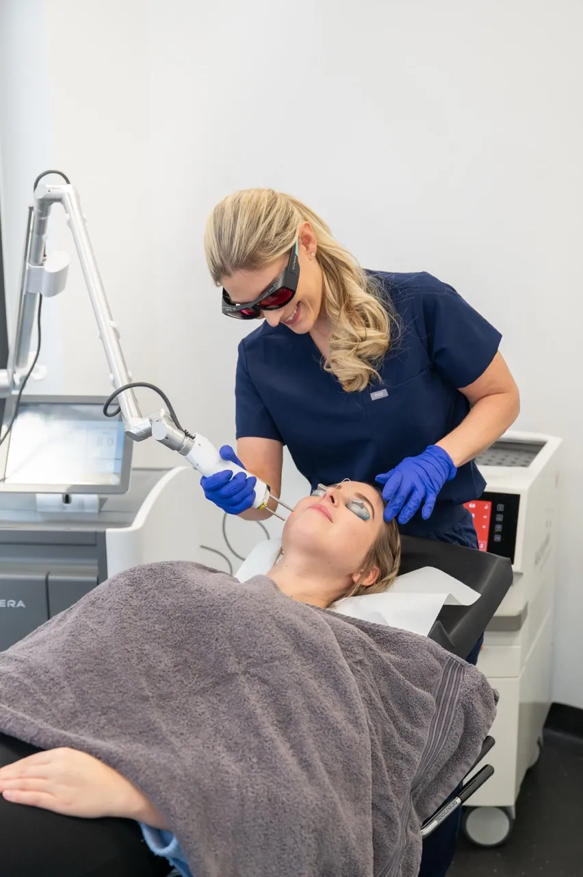 Ärztin behandelt Frau mit Lasergerät im Gesicht in moderner Klinik.