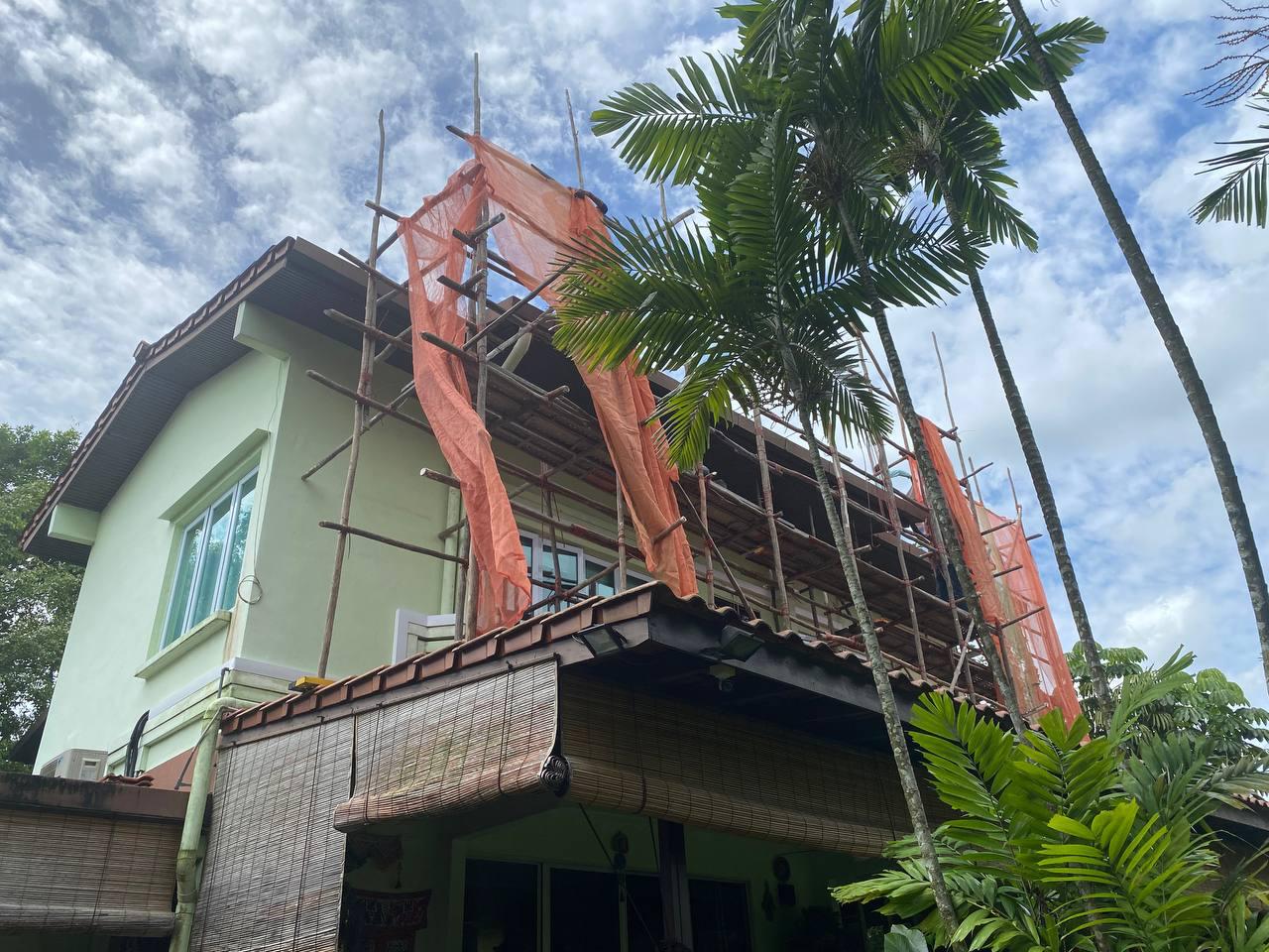 Three-story house under renovation with bamboo scaffolding and orange netting, surrounded by tall palm trees.