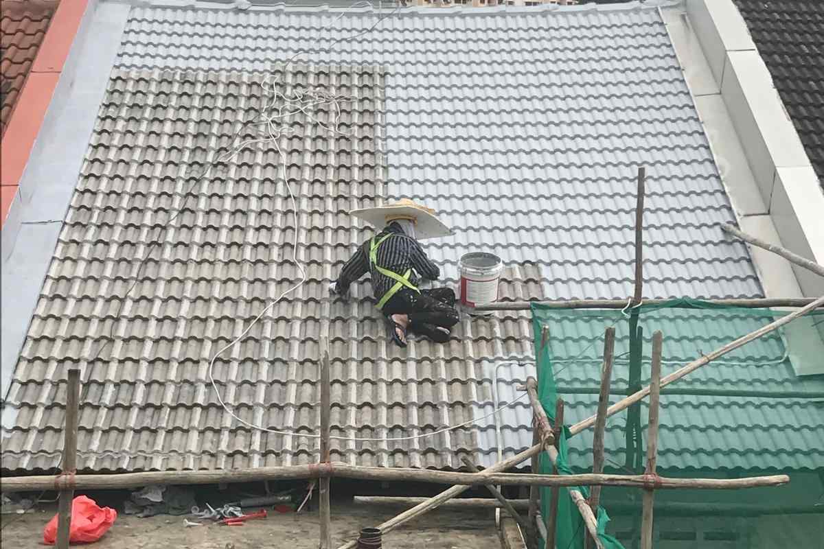 Worker in a hat painting or cleaning a tiled roof, with part of roof cleaned to lighter color.