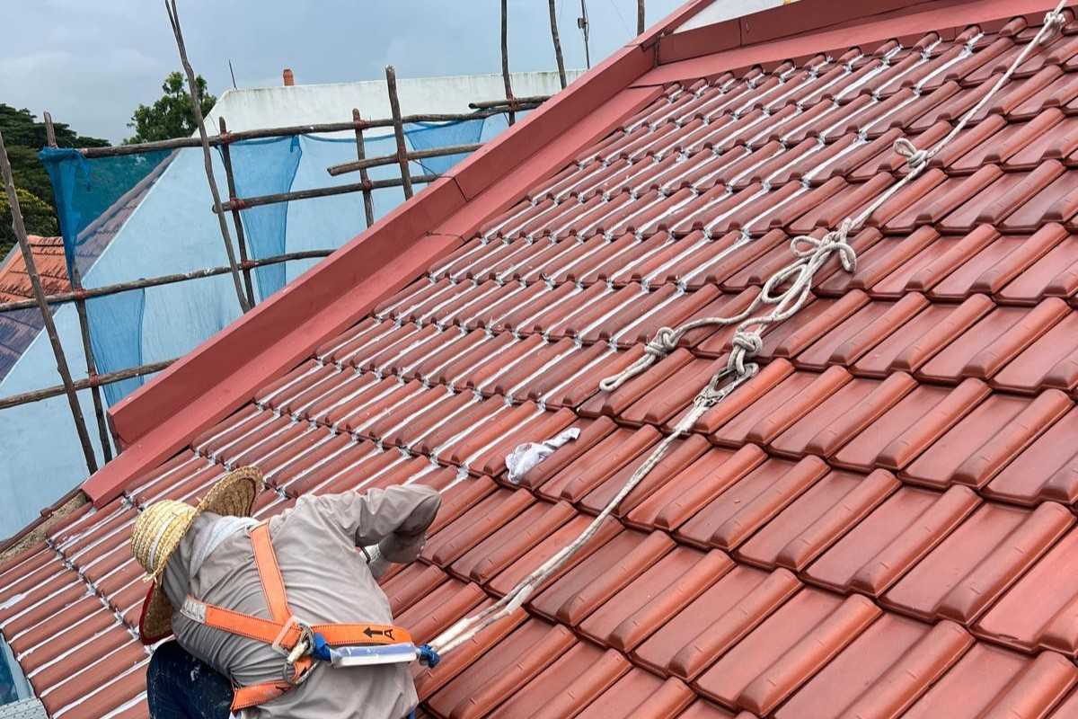 Worker in harness repairing a red tile roof with scaffolding in the background.