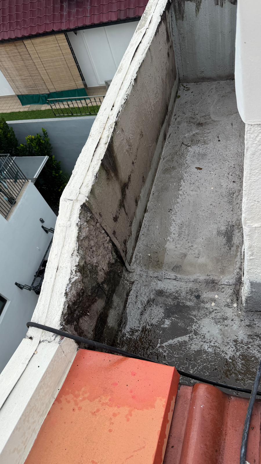 Concrete rooftop corner showing water pooling and signs of leakage or water damage on surfaces.
