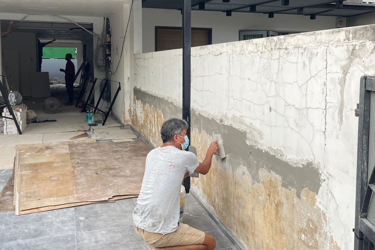 Worker patching a cracked and stained boundary wall during renovation.