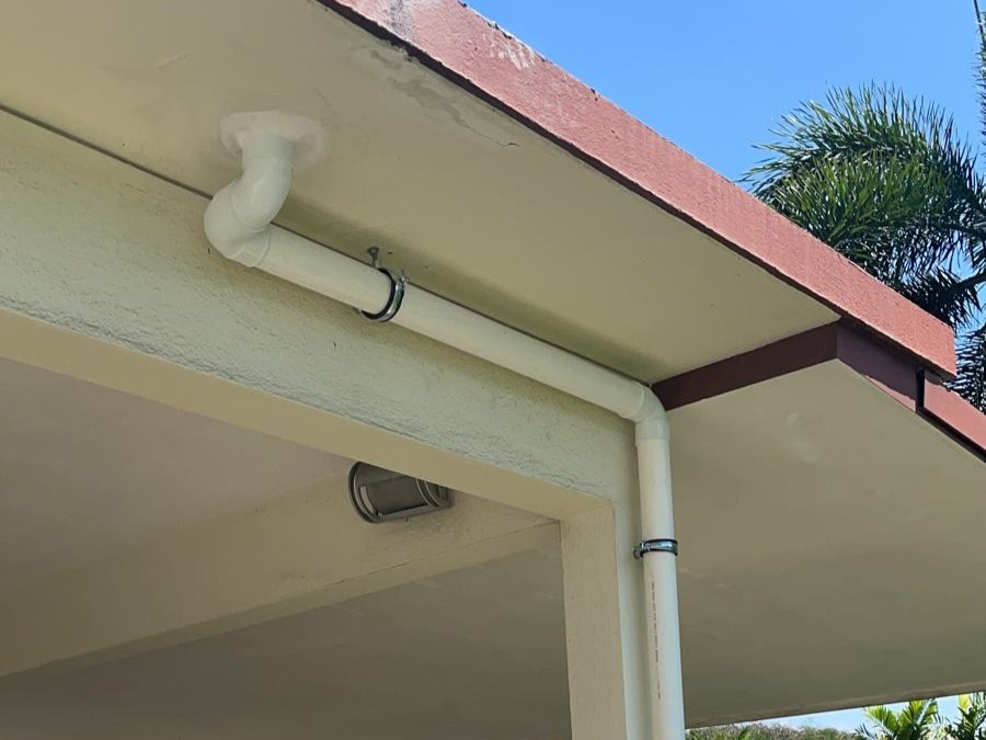 White PVC drainage pipe attached to the exterior roof corner of a building under clear blue sky.