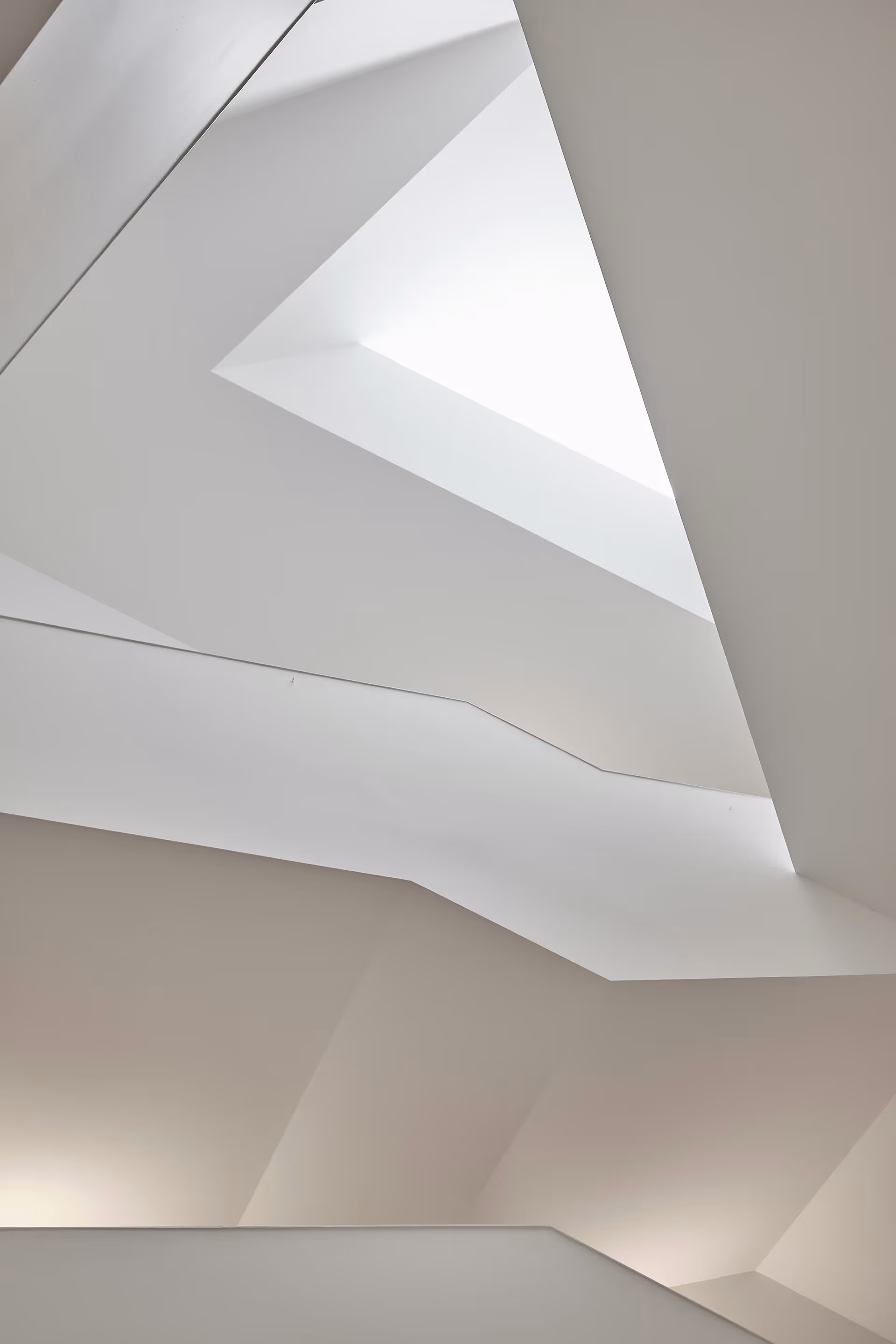 Abstrakte Innenaufnahme eines weißen, modernen Gebäudes mit geometrischen Formen und einem dreieckigen Lichtschacht im Dach.