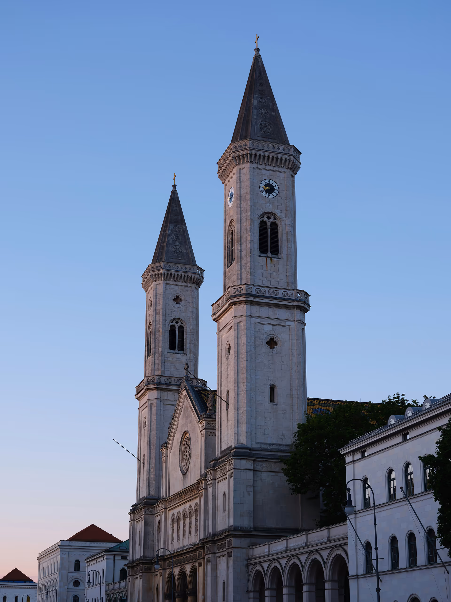 Zwei hohe Kirchtürme mit spitzen Dächern vor klarem Himmel während der Dämmerung. Theatinerkirche München.