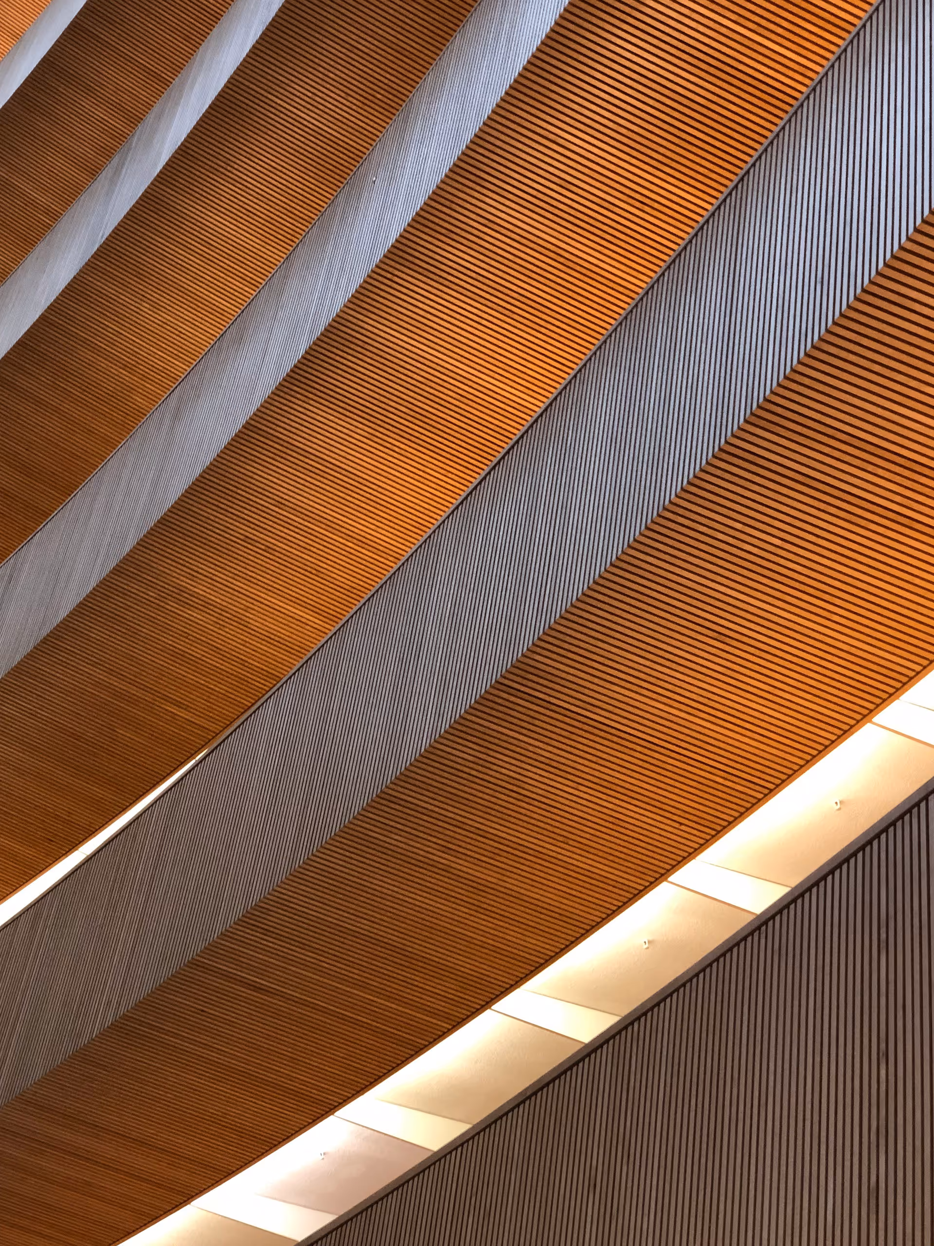 Decke mit diagonalen, abwechselnd orangefarbenen und grauen Lamellen und Beleuchtung dazwischen.