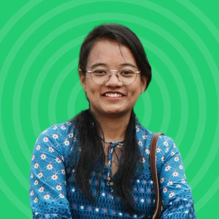 Smiling woman with glasses and long dark hair wearing a blue floral top against a green background with circular patterns.