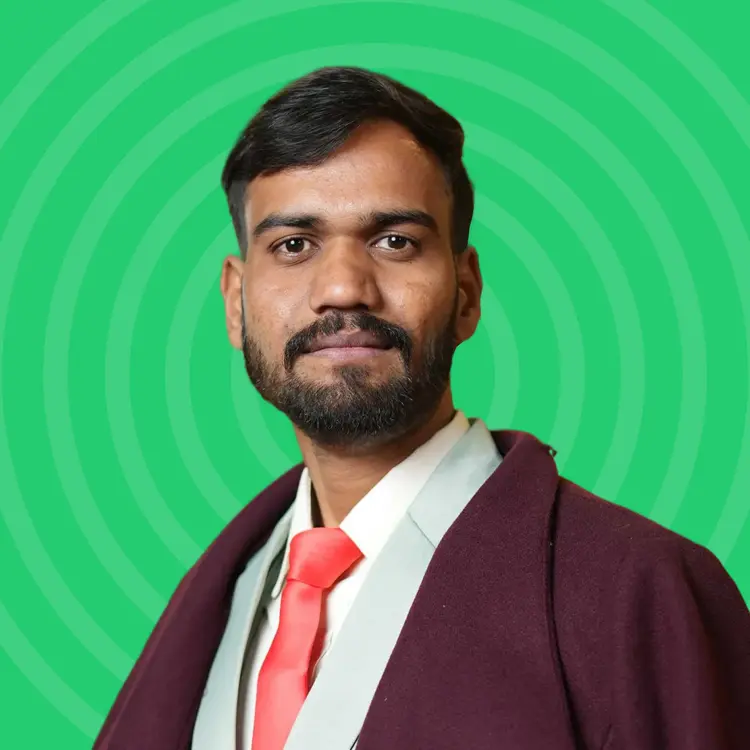 Man with dark hair and beard wearing a white shirt, orange tie, and maroon jacket on a green circular patterned background.