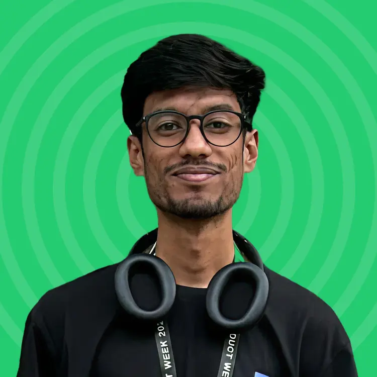 Young man with black hair and glasses wearing black headphones around his neck against a green background.