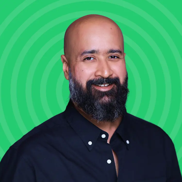Smiling bald man with a full beard wearing a black buttoned shirt against a green background with concentric circles.