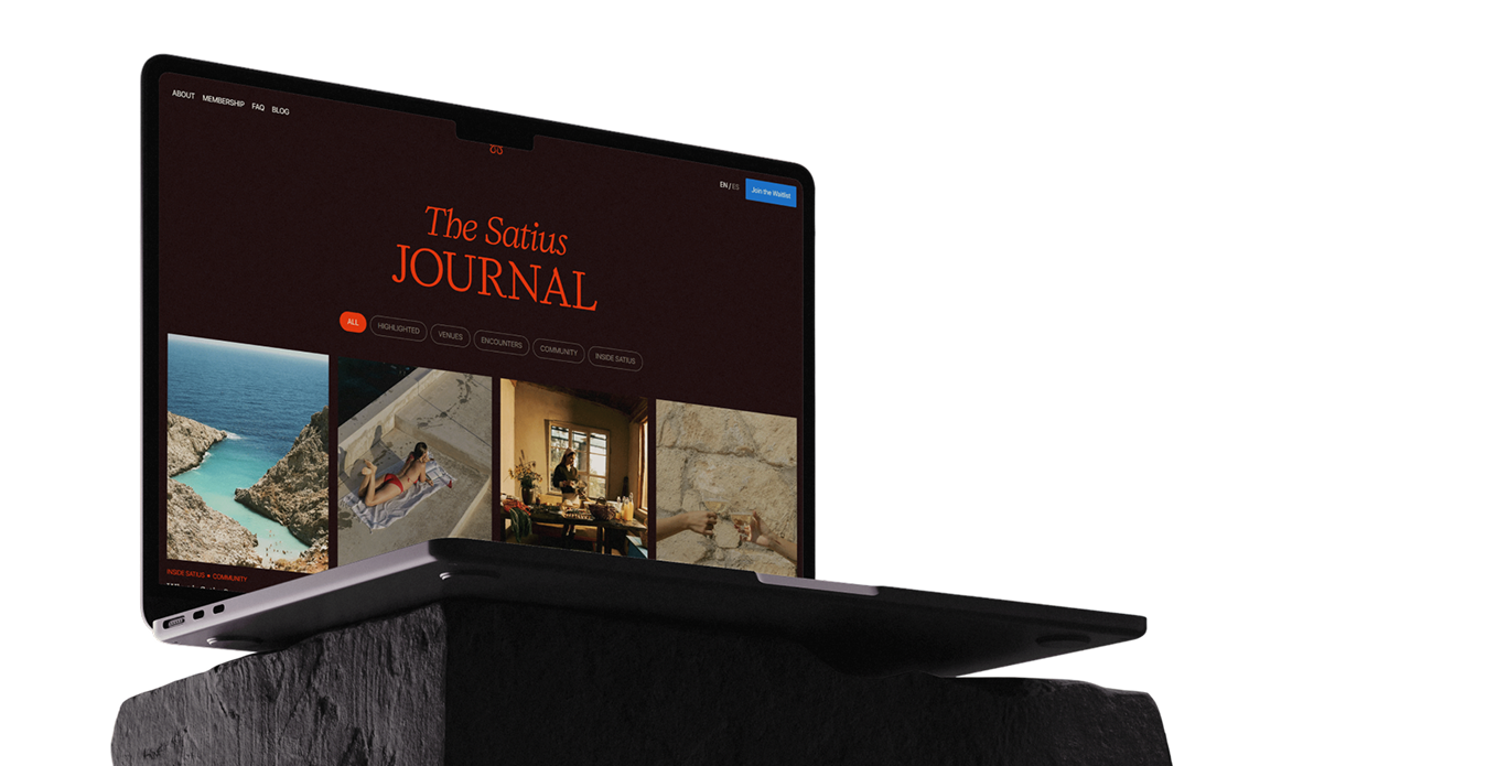 Laptop on black rock displaying The Satius Journal webpage with categories and images.